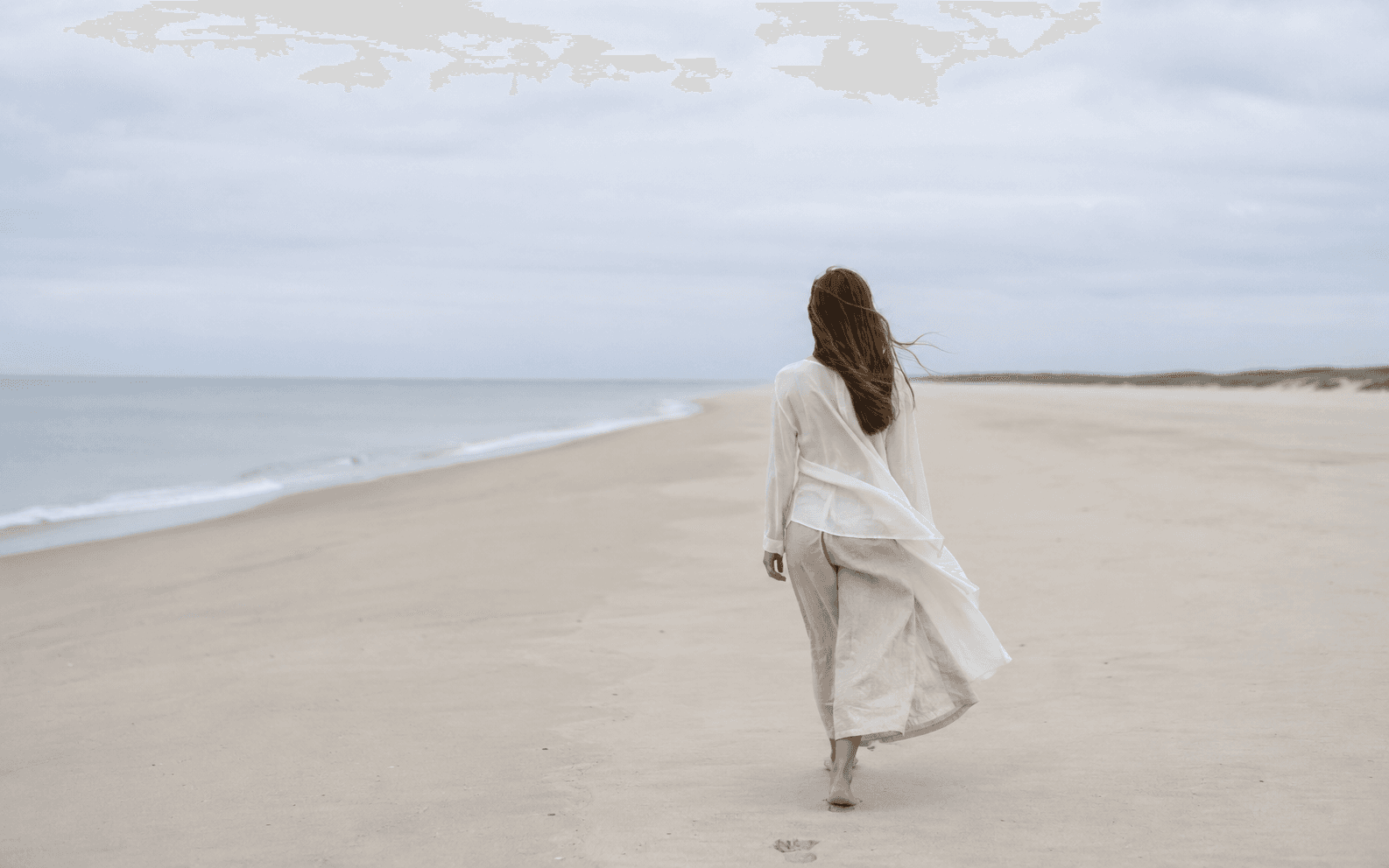 Frau geht am weiten, ruhigen Strand entlang – Sinnbild für den eigenen Weg